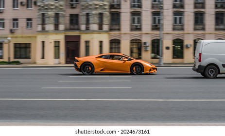 Moscow, Russia - July 2021: Orange sports car Lamborghini Huracan Evo is driving down the street. Side view of fast moving supercar car on the city highway