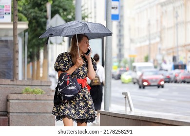 Moscow, Russia - July 2022: Girl With Umbrella Standing  On A Street And Talking On Mobile Phone On Cars Background. Rainy Weather In City, Summer Storm