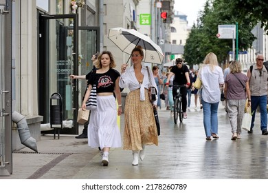 Moscow, Russia - July 2022: Two Smiling Girls With Umbrella Walking On A Street On Crowd Of People Background. Rainy Weather In City, Summer Storm