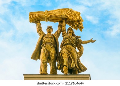 Moscow, Russia - July 21, 2021: Soviet monument "Tractor driver and сollective farm woman" on arch with main entrance to VDNH in Moscow. Goldy color monument on blue cloudy sky background.