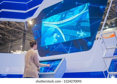 MOSCOW, RUSSIA - JUNE 05, 2019: Smart Expo. Woman using kiosk and watching presentation about Moscow industrial development on large interactive wall display at technology exhibition
