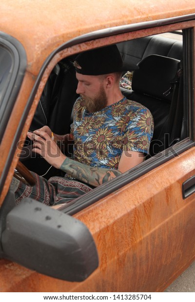MOSCOW, RUSSIA - JUNE 1, 2019: Automobile festival of\
Stance culture in Moscow city, Russia. Tuning car with imitation of\
rust and her driver - stylish man with tattoo. Cool customized car.\
Tuning car