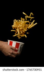 Moscow, Russia - June 16, 2020: KFC bucket (Kentucky Fried Chicken) with flying french fries in female hands, fast food. On a black background.