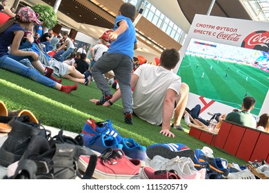 Moscow ,Russia - June 16,2018. Crowd Of People Watching A Fifa World Cup Broadcasting On Big Screen In The Large Shopping Center Mega Sitting On A Artificial Lawn Left Their Shoes Outside