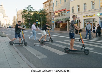 Moscow, Russia - June 18, 2021: Pedestian Crosswalk. Youth Has Sports Activity On The City Street In The Hot Summer Day. Driving Of Renting Motor Scooters. Backs. Healthy Lifestyle Concept