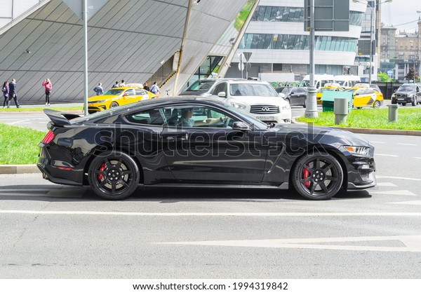 Moscow,\
Russia - June 2021: Black Ford Mustang six generation is\
accelerating in highway on urban\
background