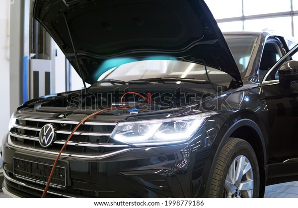 Moscow Russia - June 2021:\
Modern luxury shining black SUV car in car service. The hood of the\
machine is open and the charger is connected. Selected\
focus.
