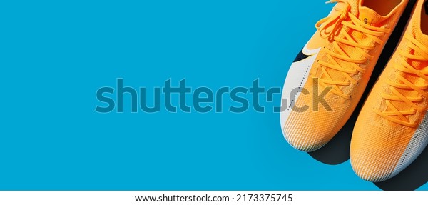 Moscow, Russia - June 2022: NIKE football\
boots shoes on blue turquoise background. Football theme wide\
banner. Pair of yellow football soccer\
cleats.
