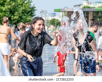 Moscow. Russia. June 26, 2021. Young girls in wet clothes are having fun and splashing in the fountain. People flee from the heat in the city fountain on a sunny summer day.