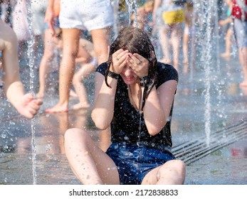 Moscow. Russia. June 26, 2021. A young girl in wet clothes sits at the bottom of a city fountain in splashes of water. People are saved from the heat in the fountain in the city in summer.