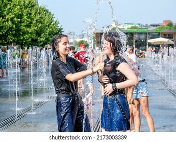 Moscow. Russia. June 26, 2021. Cheerful girls in wet clothes have fun in the water splashes of the city fountain. People flee from the heat in the city in summer.