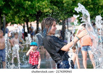Moscow. Russia. June 26, 2021. A girl in wet clothes bathes in the splashes of water from a city fountain. People flee from the heat in the city in summer.