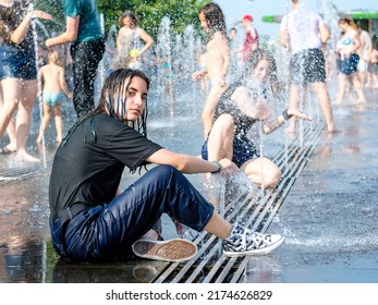 Moscow. Russia. June 26, 2021. A cute young girl in wet clothes bathes in a city fountain on a hot summer day.