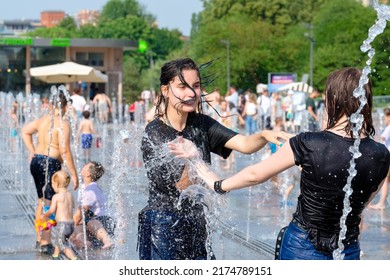 Moscow. Russia. June 26, 2021. Young girls in wet clothes are splashing in the fountain on a hot summer day. Rescue from the heat in the city in summer.