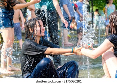 Moscow. Russia. June 26, 2021. An attractive young girl in wet clothes laughs and plays in the water jets of the city fountain on a hot summer day.