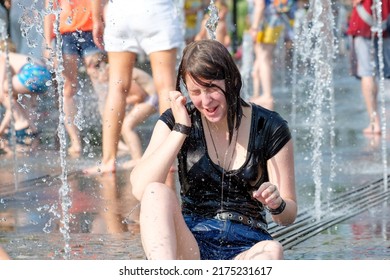 Moscow. Russia. June 26, 2021. Jets of cool water from the city fountain pour over a young girl in wet clothes. The girl sits at the bottom of the city fountain in the splashes of water.