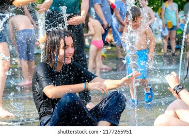 Moscow. Russia. June 26, 2021. Portrait of a beautiful young girl in wet clothes laughing and frolicking in a city fountain on a hot summer day.