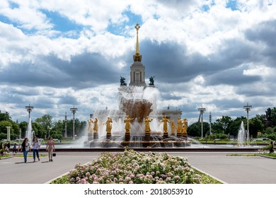 Moscow, Russia - June 30, 2021: Panoramic view of The Friendship of Nations fountain and the main entrance to VDNKh with people walking along the main alley in Moscow, Russia.