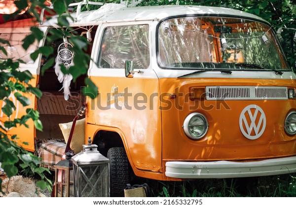 MOSCOW, RUSSIA, - JUNE 7,\
2022: Classic serfer Orange Volkswagen Camper, Van, trailer parked\
in green forest. Vacation in mobile home, picnic near the camper\
trailer.
