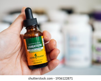 Moscow, Russia - March 09, 2021: Glass bottle with Lomatium in female hand and others nutrition supplements in blurred background. Lomatium liquid extract by Herb Pharm for Immune Support