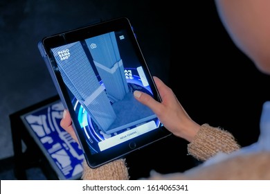 MOSCOW, RUSSIA - March 1, 2019. Woman using digital tablet device with augmented reality app and spinning virtual model of modern building in room. Future, AR, architecture and technology concept