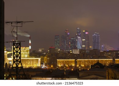 Moscow, Russia - March 13, 2022. Night Landscape With A View Of The Roofs Of Houses, An Antenna On The Roof And The Buildings Of Moscow City With Night Lights On The Horizon. For Editorial Use Only.