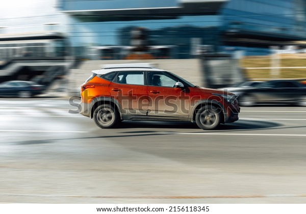 Moscow, Russia - march 2022: fast moving Kia\
Seltos crossover rides on a city road. Orange color car on street\
in motion. Overspeed in city\
concept.