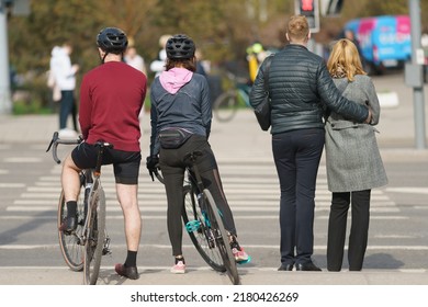 Moscow, Russia - May 2, 2022: People Are Ready To Cross Motorway By Pedestrian Crosswalk. Heterosexual Couple Hugging. Other Man And Woman Cycling. Backs, Rear View