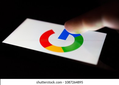 MOSCOW, RUSSIA - May 9, 2018: A smartphone lying on a table in the dark, displaying the logo of the Google. The finger above touch screen. The concept of dependence on Internet surfing.