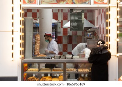 Moscow, Russia, November 30, 2020: Shop Window With Hot Baked Goods, Buns, Sandwiches And Shawarma. Chef Salesman Wraps A Purchase To A Female Shopper Standing Next To A Store