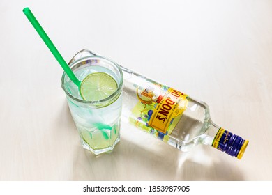 MOSCOW, RUSSIA - NOVEMBER 4, 2020: Top View Of Highball Glass With Prepared Gin And Tonic Cocktail And Lying Bottle Of Gordon's London Dry Gin On Light Brown Board. Gordon's Gin First Produced In 1769