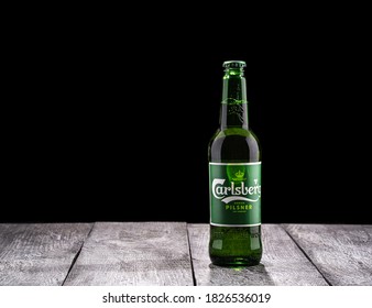 Moscow, Russia - October 1, 2020: Carlsberg pilsner bottle of beer on black background and wooden surface