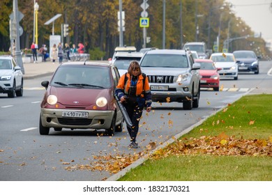 Moscow. Russia. October 11, 2020 A Woman Utility Worker Uses A Blower To Remove Fallen Leaves On A City Street. Technological Equipment. Yellow Leaves Are Flying In The Air. Seasonal Work Concept.