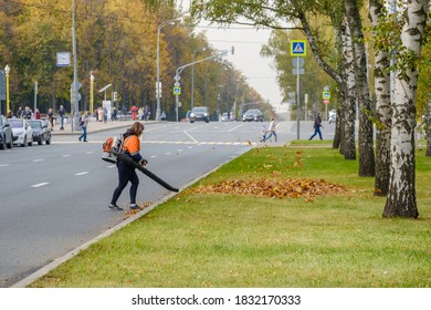 Moscow. Russia. October 11, 2020 A Woman Utility Worker Uses A Blower To Remove Fallen Leaves On A City Street. Technological Equipment. Yellow Leaves Are Flying In The Air. Seasonal Work Concept.