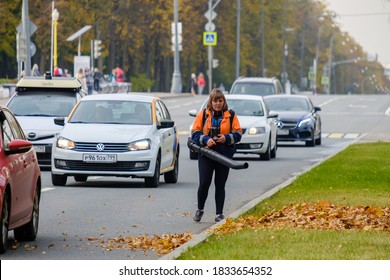 Moscow. Russia. October 11, 2020 A Woman Utility Worker Uses A Blower To Remove Fallen Leaves On A City Street. Technological Equipment. Yellow Leaves Are Flying In The Air. Seasonal Work Concept.