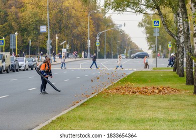 Moscow. Russia. October 11, 2020 A Woman Utility Worker Uses A Blower To Remove Fallen Leaves On A City Street. Yellow Leaves Are Flying In The Air. Cleaning Of Fallen Leaves. Seasonal Work Concept.