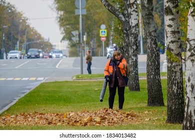 Moscow. Russia. October 11, 2020 A Woman Utility Worker Uses A Blower To Remove Fallen Leaves On A City Street. Technological Equipment. Yellow Leaves Are Flying In The Air. Seasonal Work Concept.