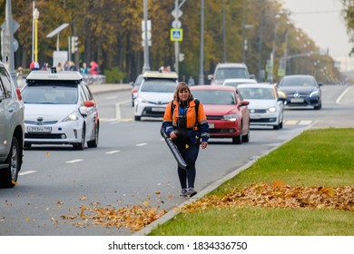 Moscow. Russia. October 11, 2020 A Woman Utility Worker Uses A Blower To Remove Fallen Leaves On A City Street. Technological Equipment. Yellow Leaves Are Flying In The Air. Seasonal Work Concept.