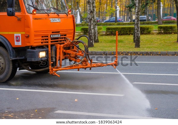 Moscow. Russia. October 11, 2020. An\
orange heavy truck washes autumn leaves off the asphalt street. The\
work of public utilities in the city. Autumn\
day.