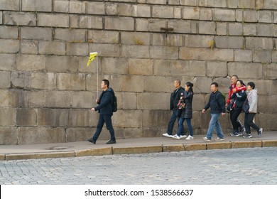 Moscow, Russia - October 18, 2019: Photography Of A Group Of Chinese Tourists, Leds By A Guide With Yellow Flag, Head For A Tour Of Red Square In Autumn Day. Touristic Concepts.