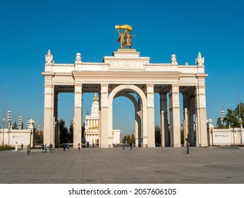 Moscow, Russia - October 5, 2021: Arch of the main entrance of VDNKh against the background of the blue sky. People walk on an autumn sunny day in the square near the entrance to the park.