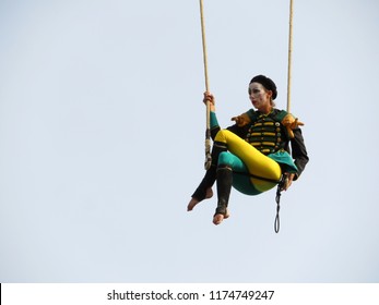 Moscow, Russia - September 2018: Woman air gymnast sitting on trapeze isolated on sky background during a street performance of french circus "Transe Express" (Les Tambours) on the day of Moscow