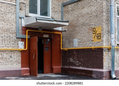 Moscow, Russia - September, 26, 2022. An Open Brown Entrance Door In An Ordinary City Apartment Building. The Wall Is Made Of Gray Brick With The House Number Written In Paint. Paper Ads On Entrance.