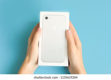 Moscow, Russia-July 14, 2018: Woman Holding A Box Of Apple IPhone Smartphone On A Blue Background. Unboxeind Concept With Copy Space.