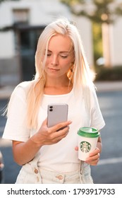 Moscow/Russia 03 August, 2020: Young Woman Holding Iphone 11 In Purple Shade And Starbucks Paper Cup Of Coffee In City Street Outdoors Closeup In Sun Light. 