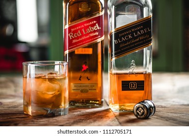 MOSCOW/RUSSIA - APRIL 24, 2018: Red label and Black label whiskey bottles and glass with ice cubes on wooden table. Johnnie Walker is Scotch blended whiskey and one of famous brands in world