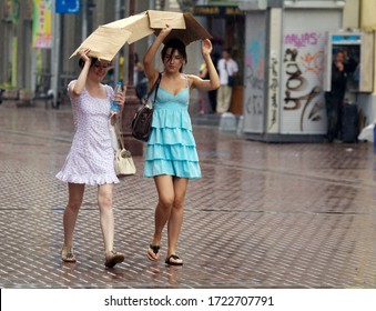 Moscow/Russia - August, 05, 2012: Two Beautiful Young Joyful Girls Walk Down Arbat Street In Moscow City Under Summer Rain, Sheltering With A Box