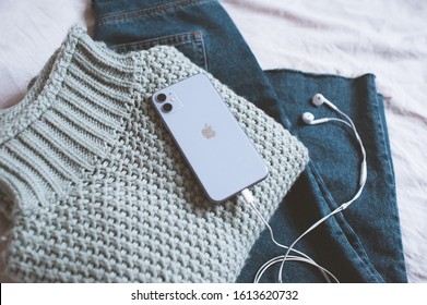 Moscow/Russia - January 12, 2020: Iphone 11 With Dual Camera And Headphones On Casual Sweater And Denim Pants Closeup In Bed. 