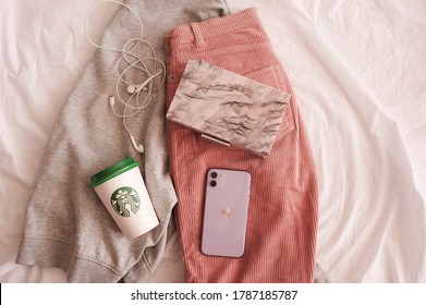 Moscow/Russia - July 23, 2020: Iphone 11 In Purple Shade With Starbucks Coffee Cup And Stylish Bag On Clothes In Bed Closeup. Top View. 