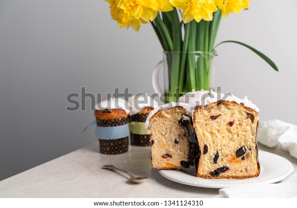 Moscow/Russia-CIRCA 03.2018: an\
image of Easter cakes, cut in half, inside of the cake are dry\
fruits, on a white plate, yellow daffodils on background, grey wall\
background